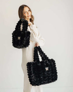 Woman holding two sizes of Annie Bag Ripple Black, showcasing luxurious style and versatility in a chic setting.