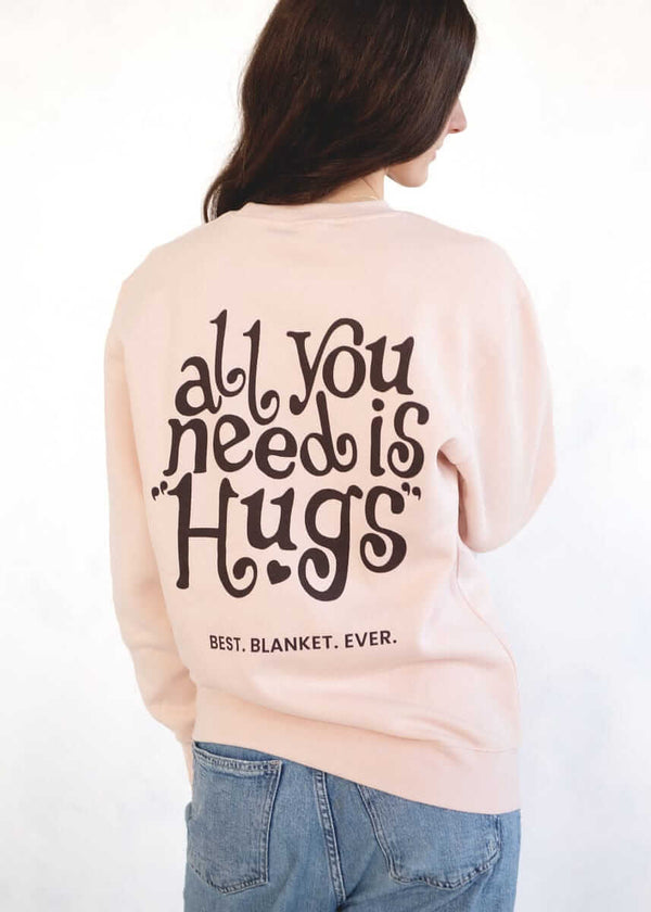 Person wearing a light pink Minky Couture sweatshirt with “All You Need Is Hugs” text on the back.