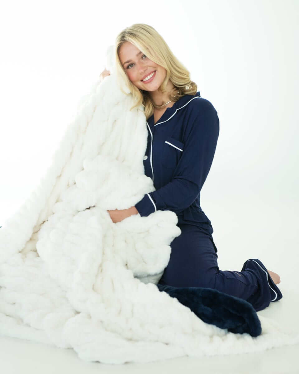 Woman in Navy Evening Blue Middle of the Night Pajamas kneeling and holding a soft chunky white knit blanket.