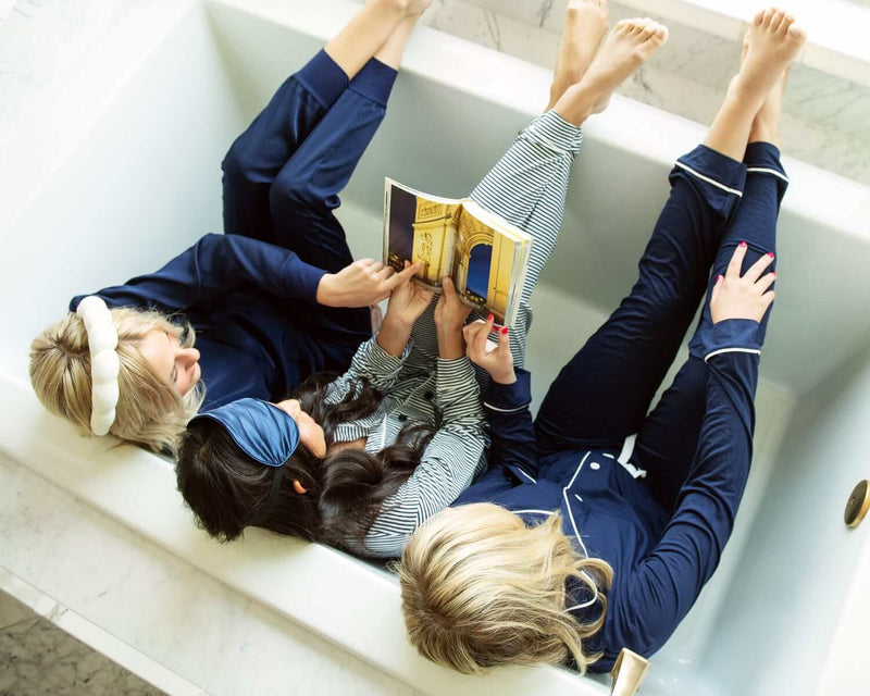 Three people in Minky Couture Middle of the Night Pajamas relaxing in a bathtub, reading a book together.