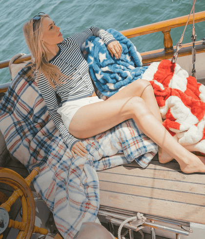 Woman lounging on a boat with striped shirt and cozy blankets by the water.