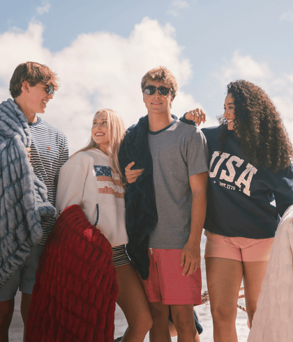 Group of friends at a beach, wearing casual summer outfits and enjoying a sunny day with colorful blankets.