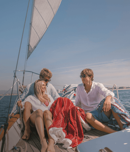 Three friends enjoying a sunny day on a sailboat, relaxing with a blanket and ocean views.