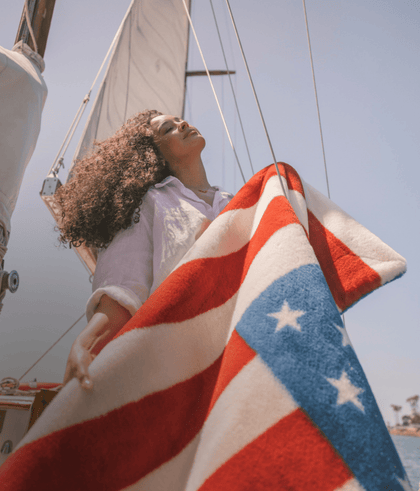 Woman on a boat holding a star-patterned blanket against a clear sky, creating a vibrant maritime scene.
