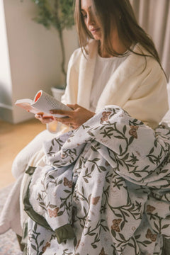 Woman sitting on a couch with a floral blanket, holding a magazine.