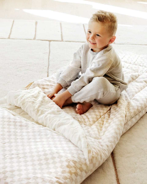 Smiling boy sitting on a beige Oat checkered Minky Couture blanket.