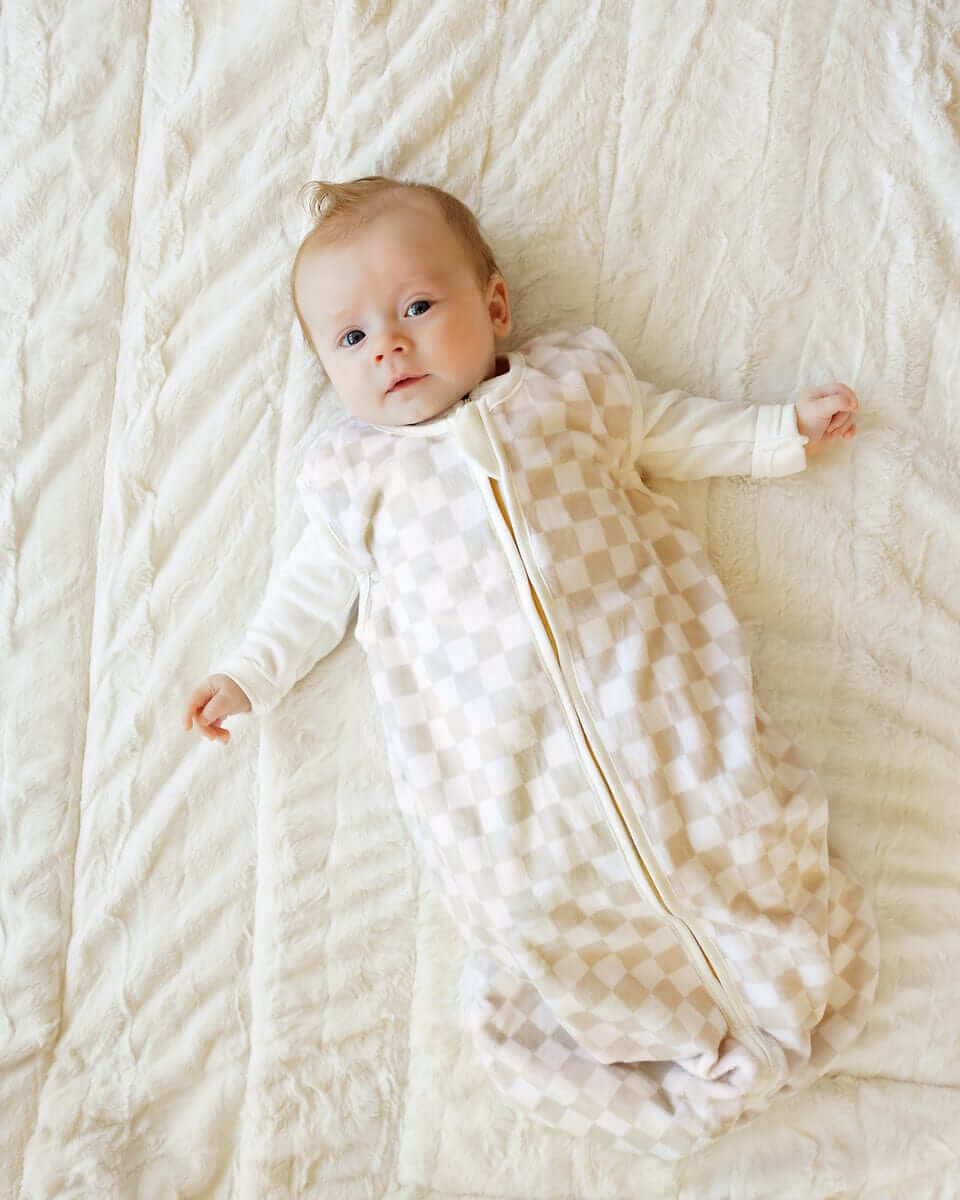 Baby lying on a soft cream blanket, with a Oat Check Wearable Minky Blanket.