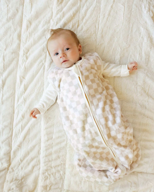 Baby lying on a soft cream blanket, with a Oat Check Wearable Minky Blanket.