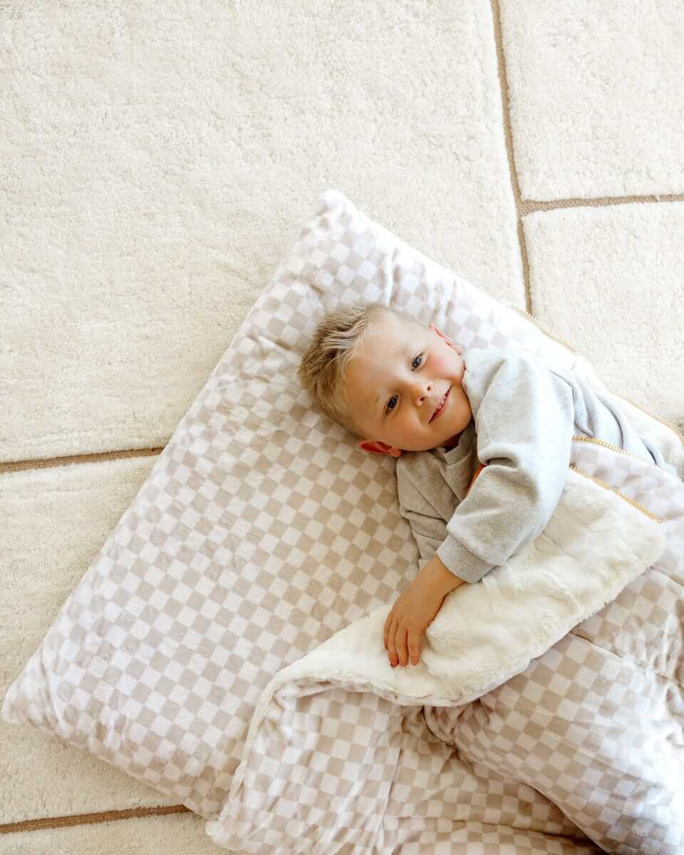 Smiling boy lying under a beige Oat checkered Minky Couture blanket.