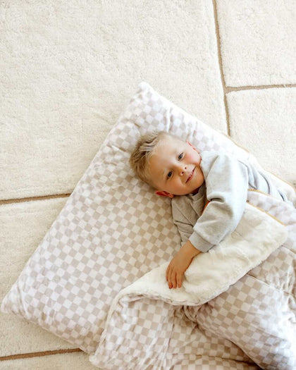 Smiling boy lying under a beige Oat checkered Minky Couture blanket.