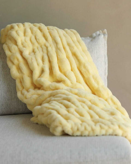 Hugs Butter Yellow Blanket draped elegantly on a soft couch, showcasing its plush and cozy texture.