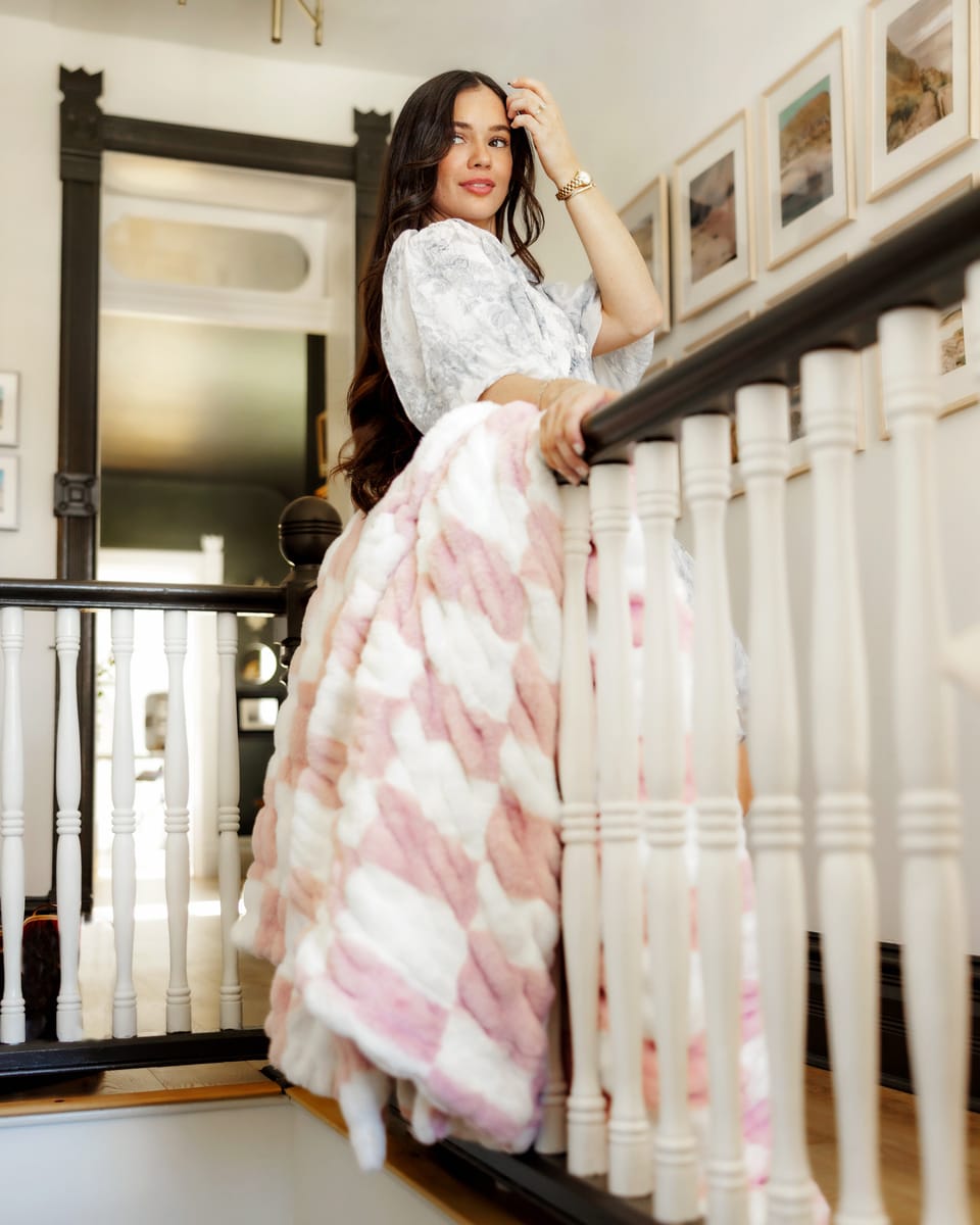 Stylish woman draped in the Hugs Check Pink Blanket, showcasing its charming checkered pattern in a cozy home setting.