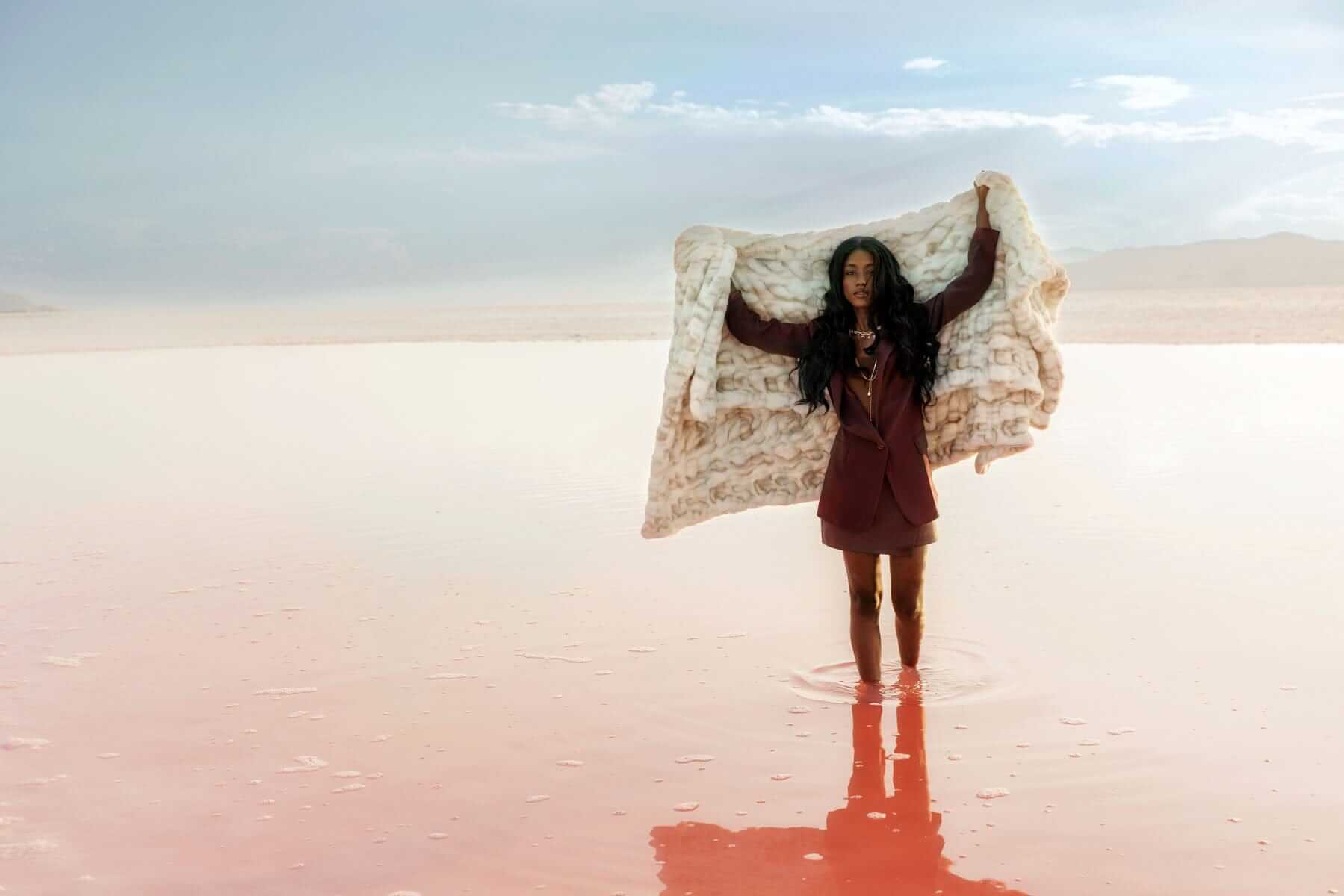 A woman holding the Hugs Marble Sand Blanket while standing in water, showcasing the blanket's elegance and comfort.
