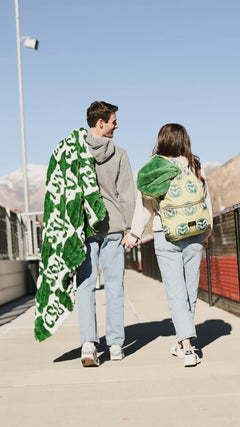 Couple standing on stadium bleachers wrapped in a green and white Minky Couture CSU blanket.