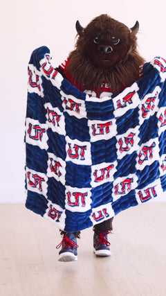 Utah Tech mascot holding blue and white Minky Couture UT checkered plush blanket.