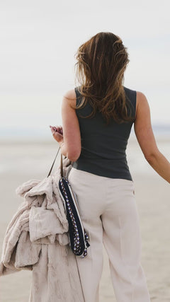 Woman walking on the beach holding a Sorbet Almond Croissant Blanket with a casual outfit.
