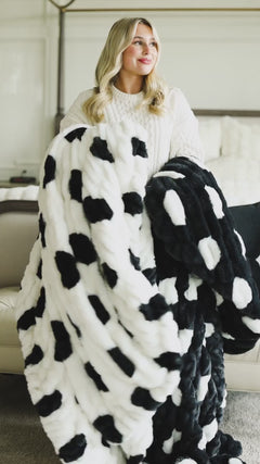 Woman holding a black-and-white chunky blankets with polka dots pattern.