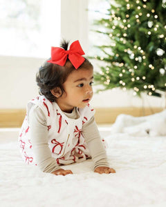 Baby girl on a soft carpet, next to a Christmas tree,  with a Minky Couture red ribbon wearable blanket.