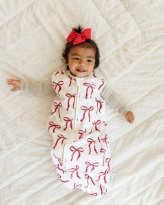 Smiling baby girl lying on a bed with Minky Couture red ribbon wearable blanket.