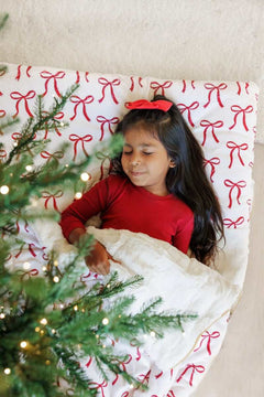 Young girl in a white and red bow-patterned Minky Couture sleeping bag.