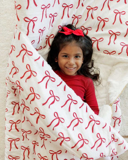 Girl in red wrapped in a white Minky Couture sleeping bag with red bows.