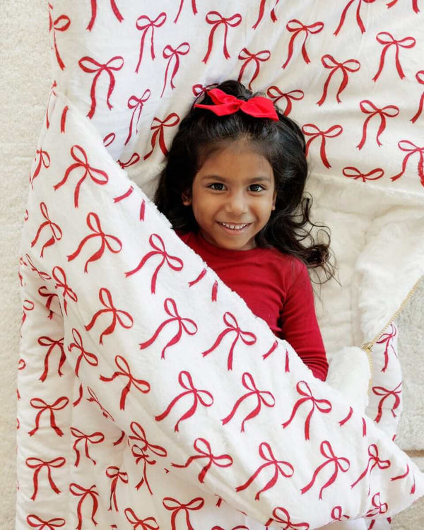 Girl in red wrapped in a white Minky Couture sleeping bag with red bows.