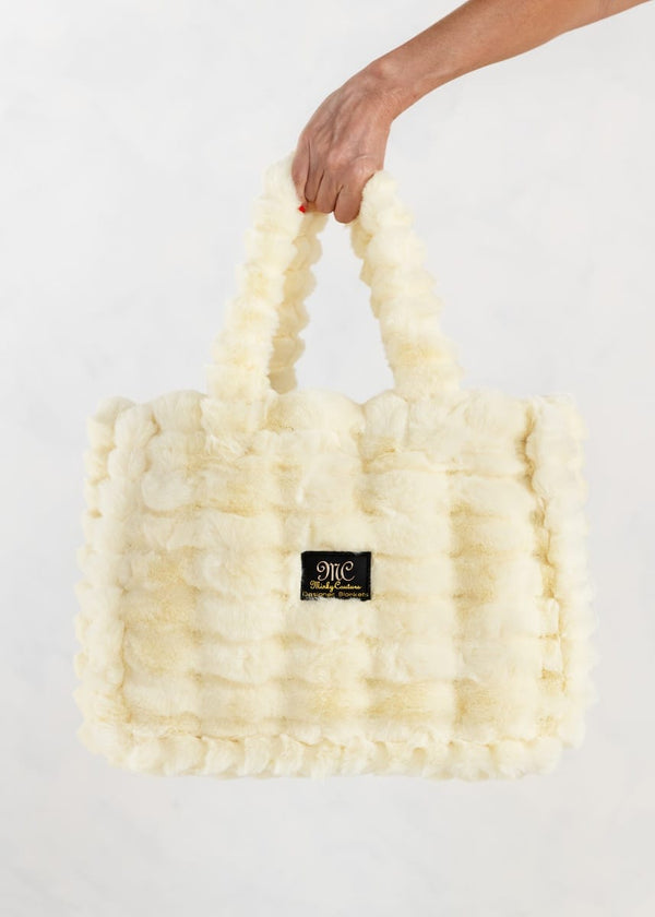 A butter yellow colored, textured faux fur tote bag with a small black "MC" Minky Couture brand patch on the front, held by a hand against a plain white background.