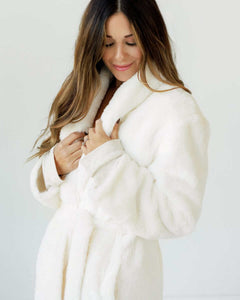 Woman wearing a luxurious cream robe with a plush collar and ties, enjoying its comfort.