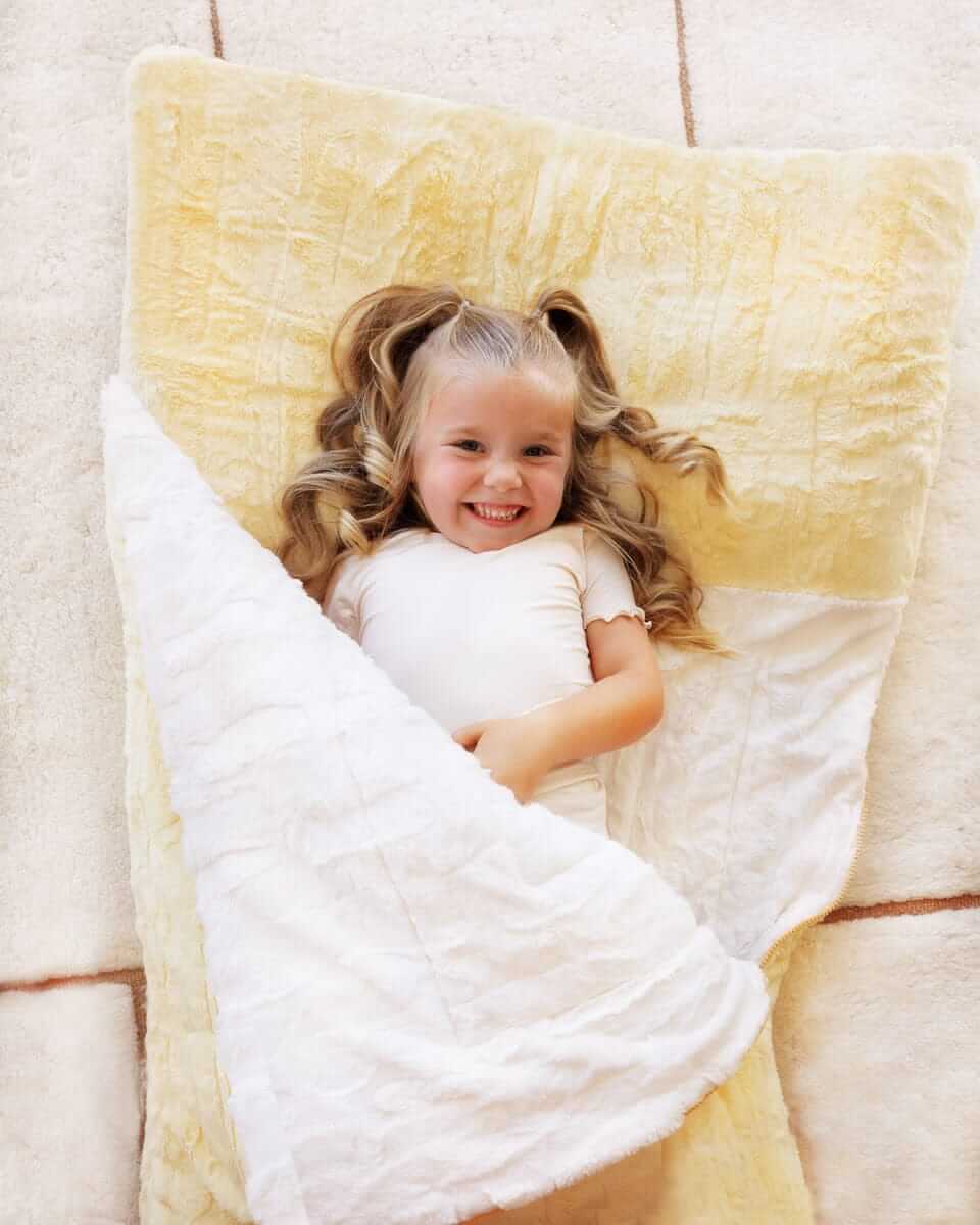 Girl laying down happy on Minky Couture Sleeping Bag Butter Yellow.