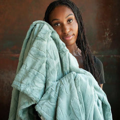 A woman holds the soft, plush Sorbet Mist Blanket, showcasing its gentle green hue and textured feel.