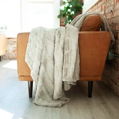 Beige gray blanket draped over an brown chair in a room with a brick wall and plant.