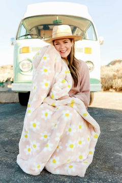 Smiling woman wrapped in Minky Couture Lush Peach Flower Blanket with daisies, sitting in front of a vintage van.