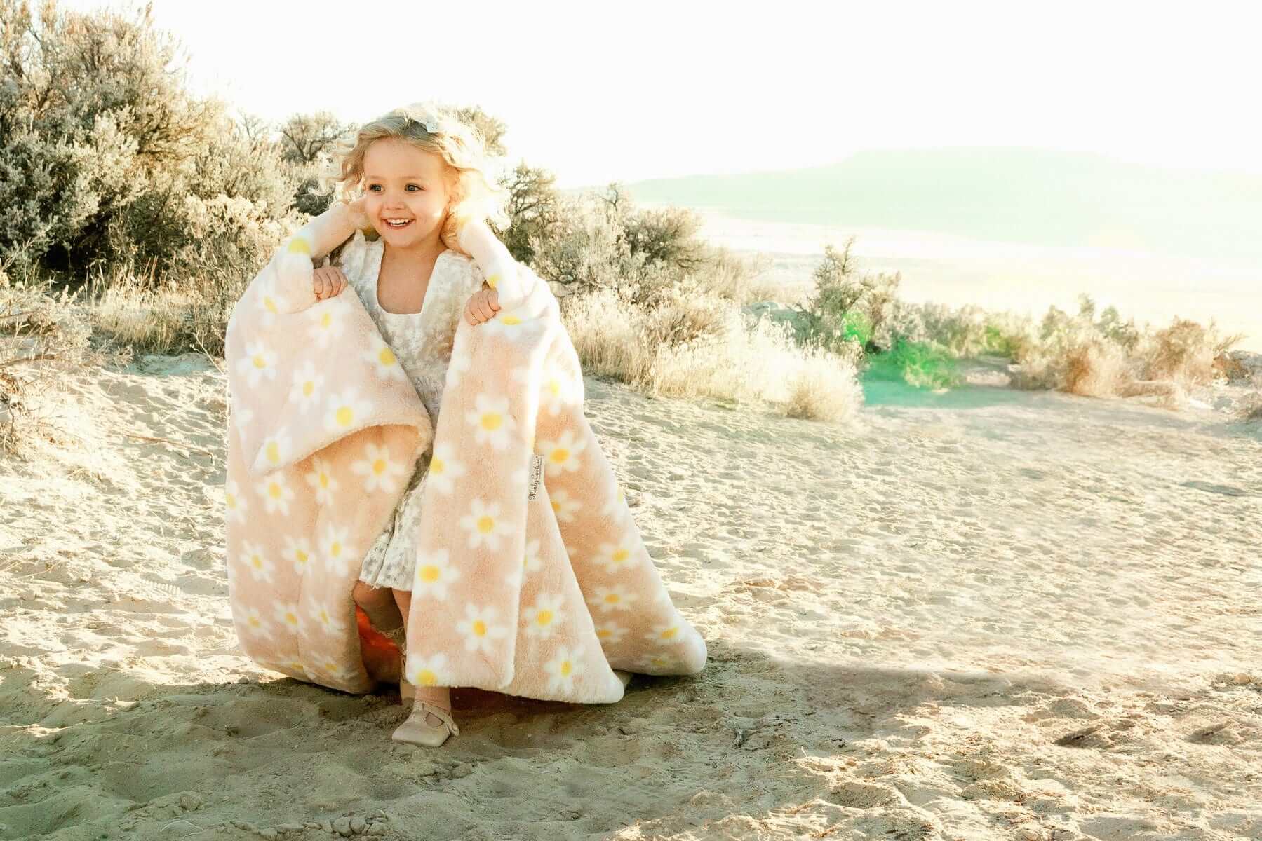 A joyful child wrapped in the Lush Peach Flower Blanket, showcasing its playful daisy prints on a warm peach background.