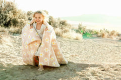 A joyful child wrapped in the Lush Peach Flower Blanket, showcasing its playful daisy prints on a warm peach background.