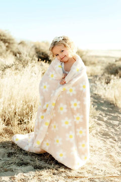 Lush Peach Flower Blanket wrapped around a smiling child outdoors, featuring floral daisies on a soft peach background.