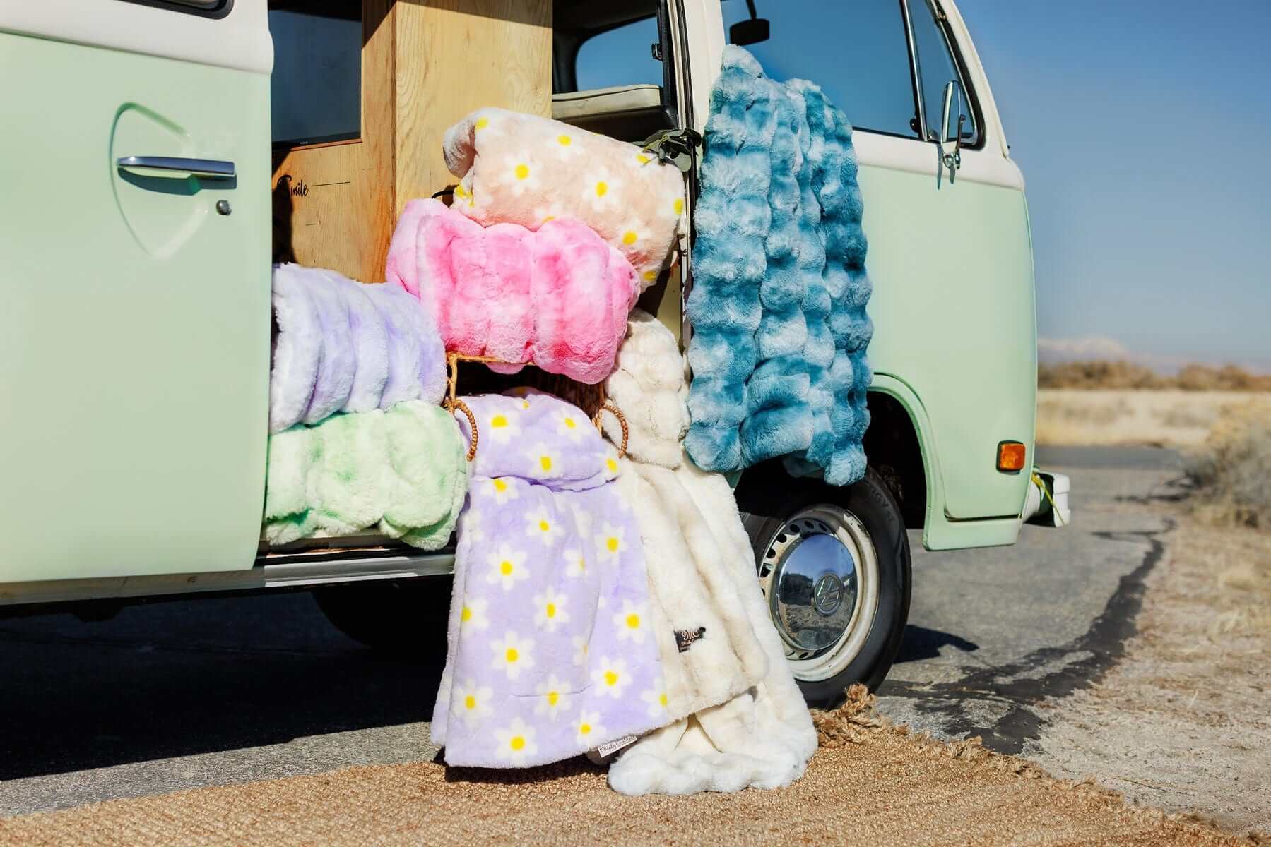 Lush Flower Blankets displayed among colorful weighted blankets near a vintage van in a picturesque outdoor setting.