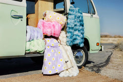 Lush Flower Blankets displayed among colorful weighted blankets near a vintage van in a picturesque outdoor setting.