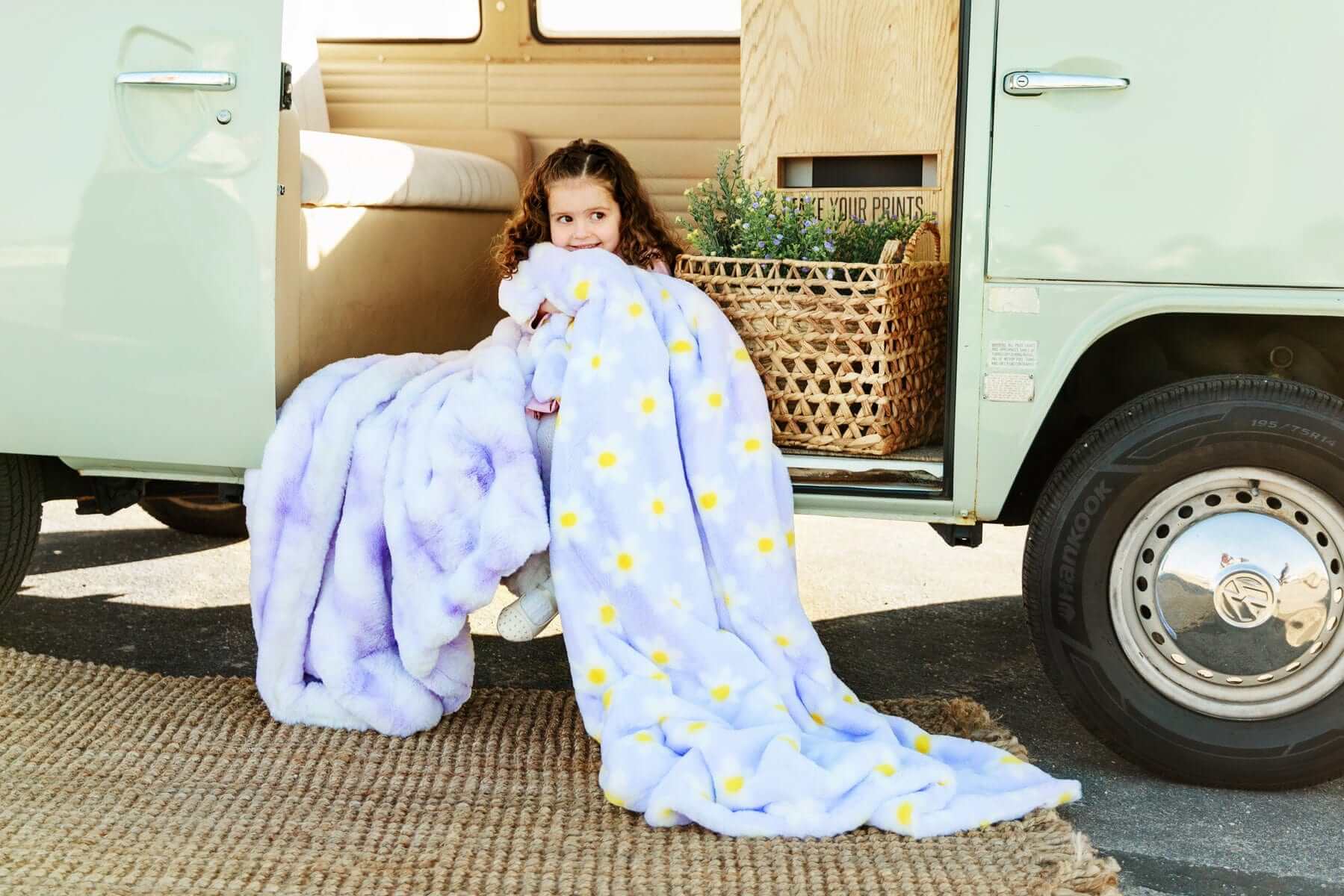 Child wrapped in Minky Couture Lush Lilac Flower Blanket with playful floral design by a vintage van.