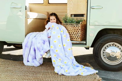 Child wrapped in Minky Couture Lush Lilac Flower Blanket with playful floral design by a vintage van.