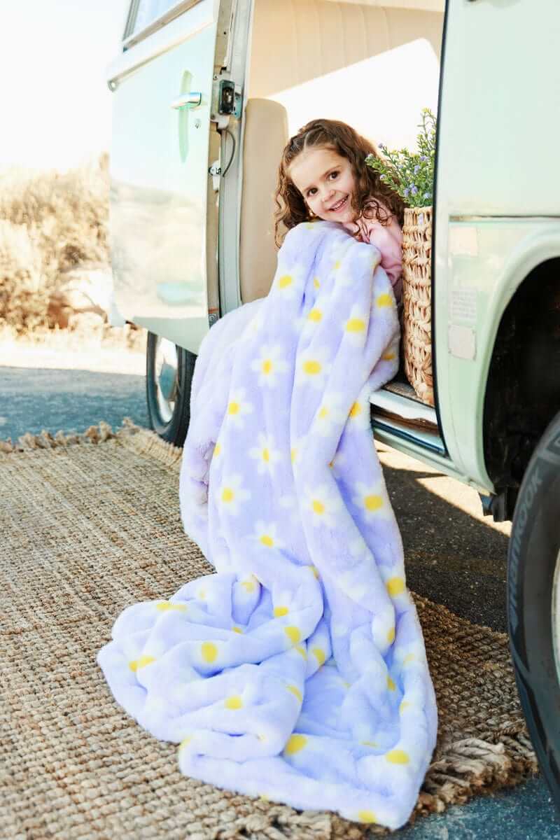 Child wrapped in Lush Lilac Flower Blanket with daisies, sitting by a vintage vehicle, enjoying outdoor coziness.