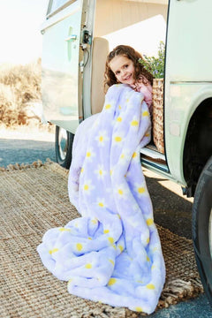 Child wrapped in Lush Lilac Flower Blanket with daisies, sitting by a vintage vehicle, enjoying outdoor coziness.