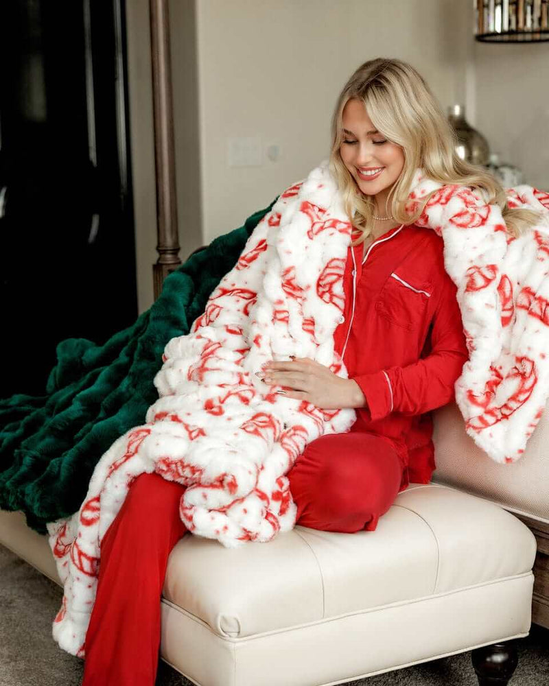 Woman sitting with a green and a white and red peppermint Hugs Candy Cane blankets