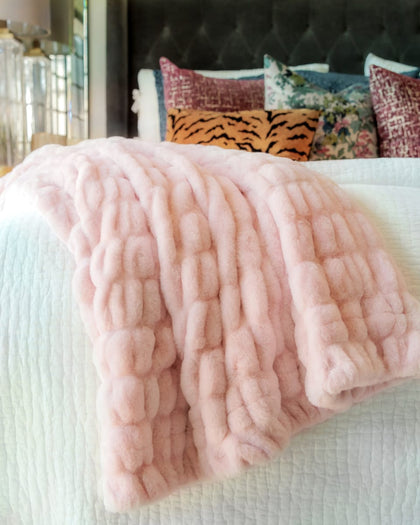 Pink textured blanket on a bed with colorful pillows in the background
