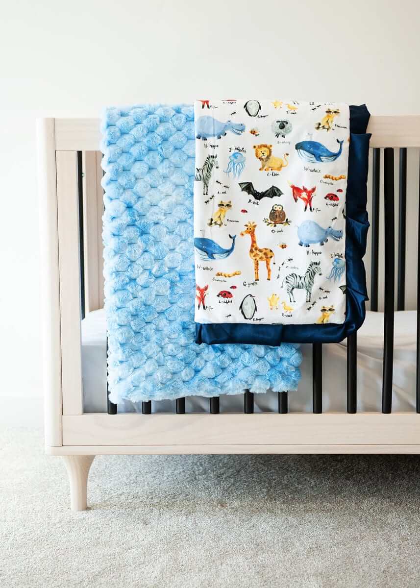 ABC Zoo Light blue textured blanket and zoo animal themed blanket over the edge of a crib. 
