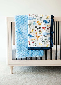 ABC Zoo Light blue textured blanket and zoo animal themed blanket over the edge of a crib. 