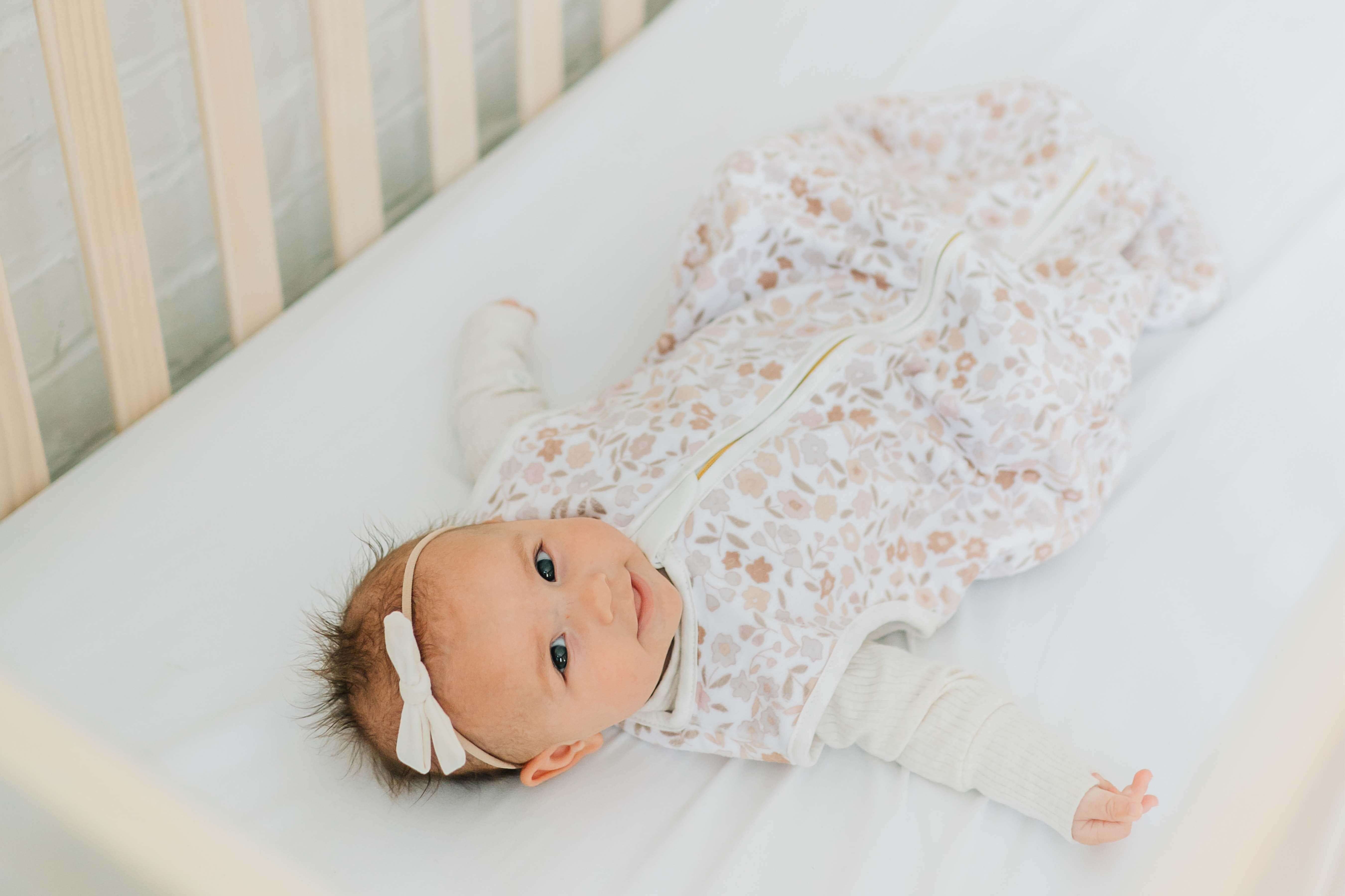 Dainty Floral Wearable Minky Blanket displayed with a happy baby in a crib, showcasing its floral design and gold zipper.
