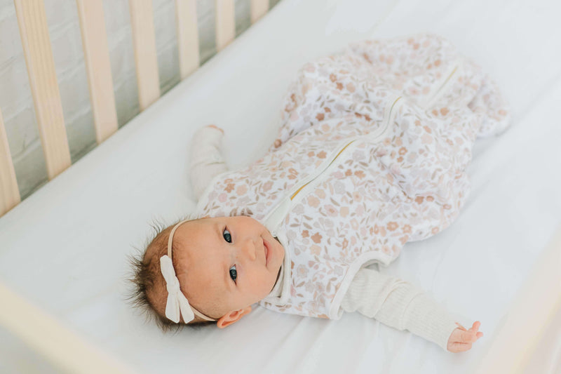 Dainty Floral Wearable Minky Blanket displayed with a happy baby in a crib, showcasing its floral design and gold zipper.