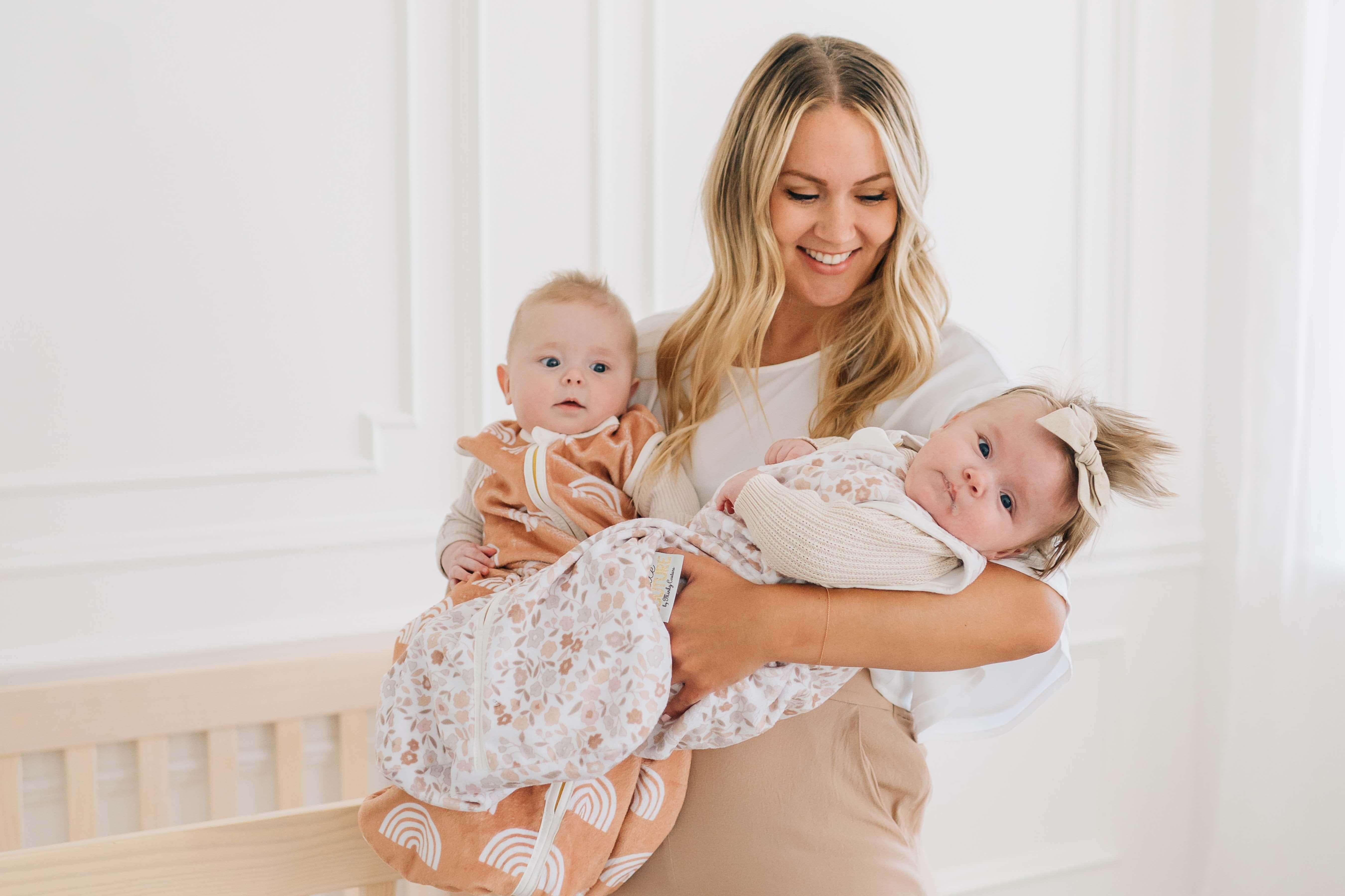 Mom holding two babies in Dainty Floral Wearable Minky Blankets, showcasing soft designs with floral patterns.