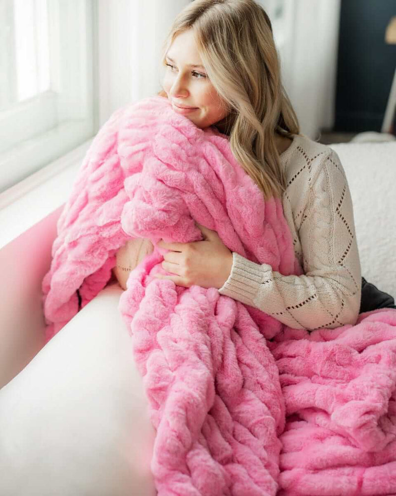 Young woman holding a hot pink ruched plush blanket near her face.