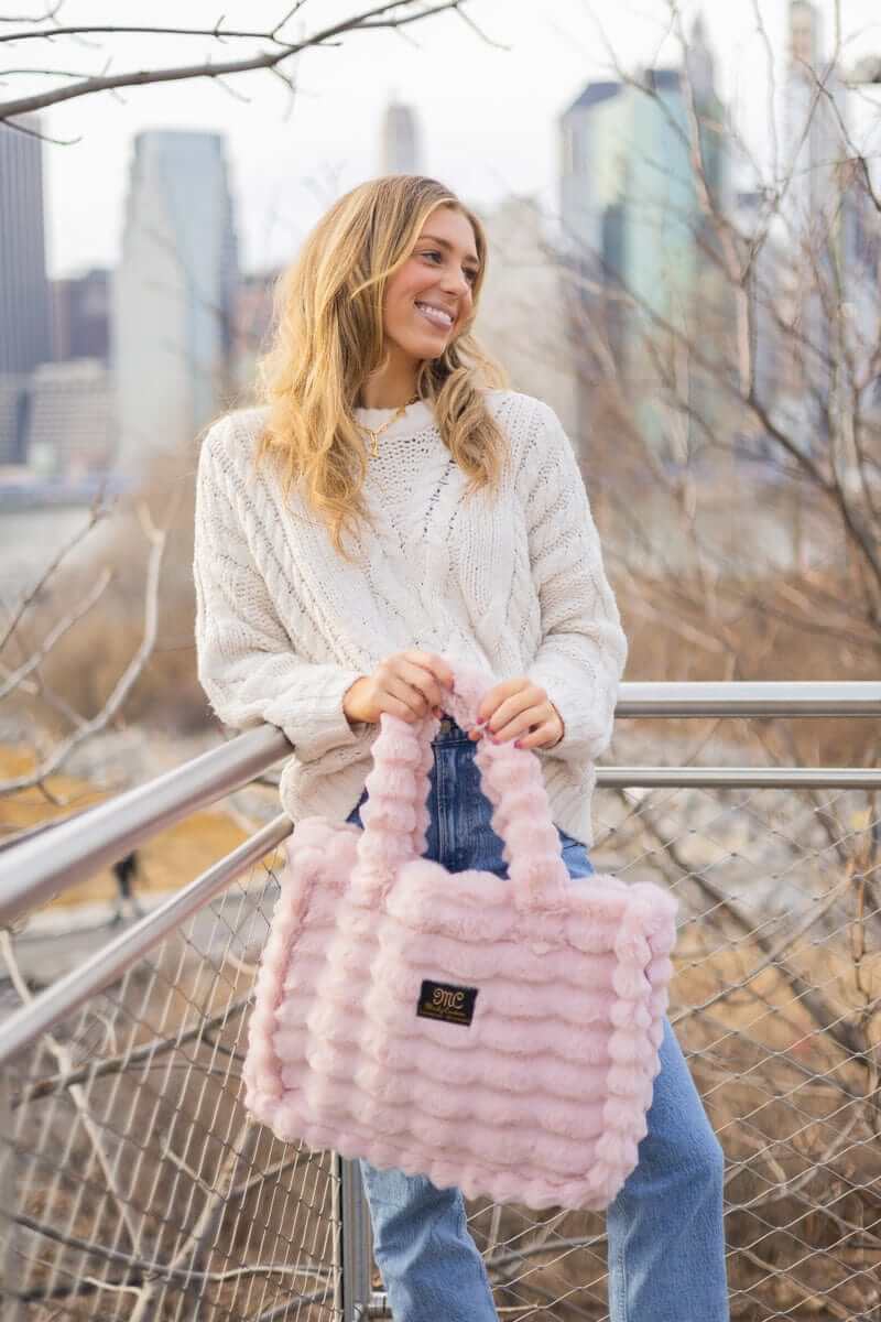 Woman showcasing the Annie Bag Ripple Blush while wearing a cozy sweater, set against a vibrant city backdrop.